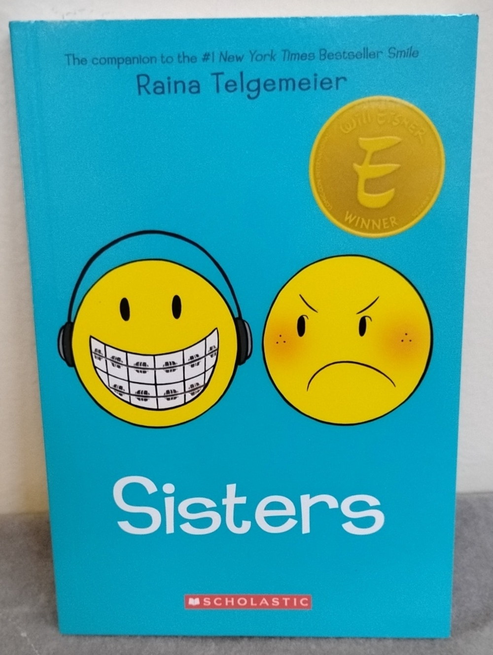 D- Sisters by Raina Telgemeier — Bright Teal Cover with Yellow Emojis